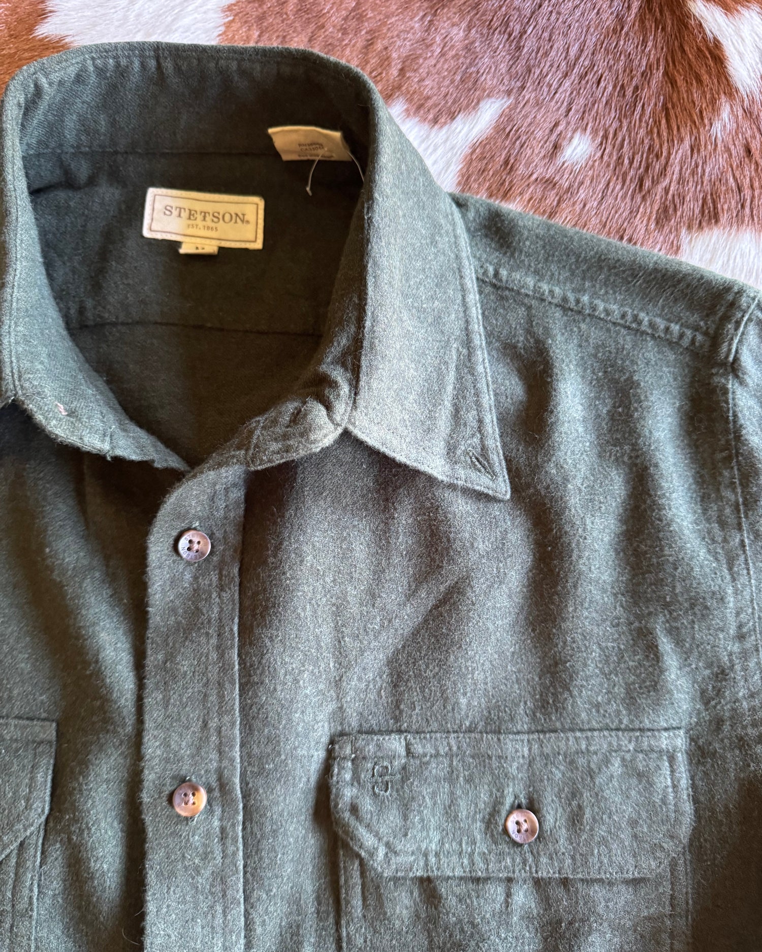 Green flannel shirt with a visible brand tag on a brown and white surface