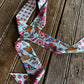 A long scarf with a colorful floral and paisley pattern on a light blue base, laid out on a rustic wooden plank surface.