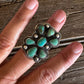A close-up of a hand wearing a large silver ring set with multiple oval turquoise stones, resting on a rustic wooden surface.