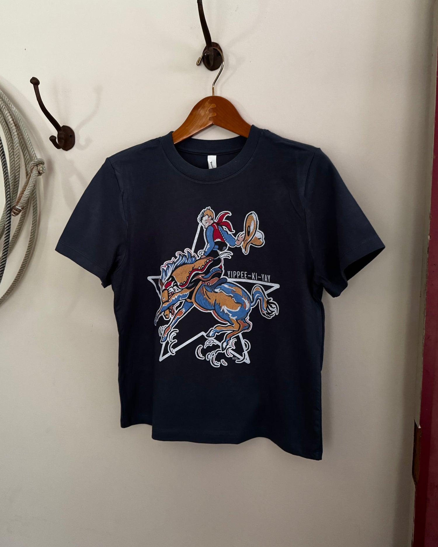 Navy blue t-shirt with graphic design on a wooden hanger against a white wall.