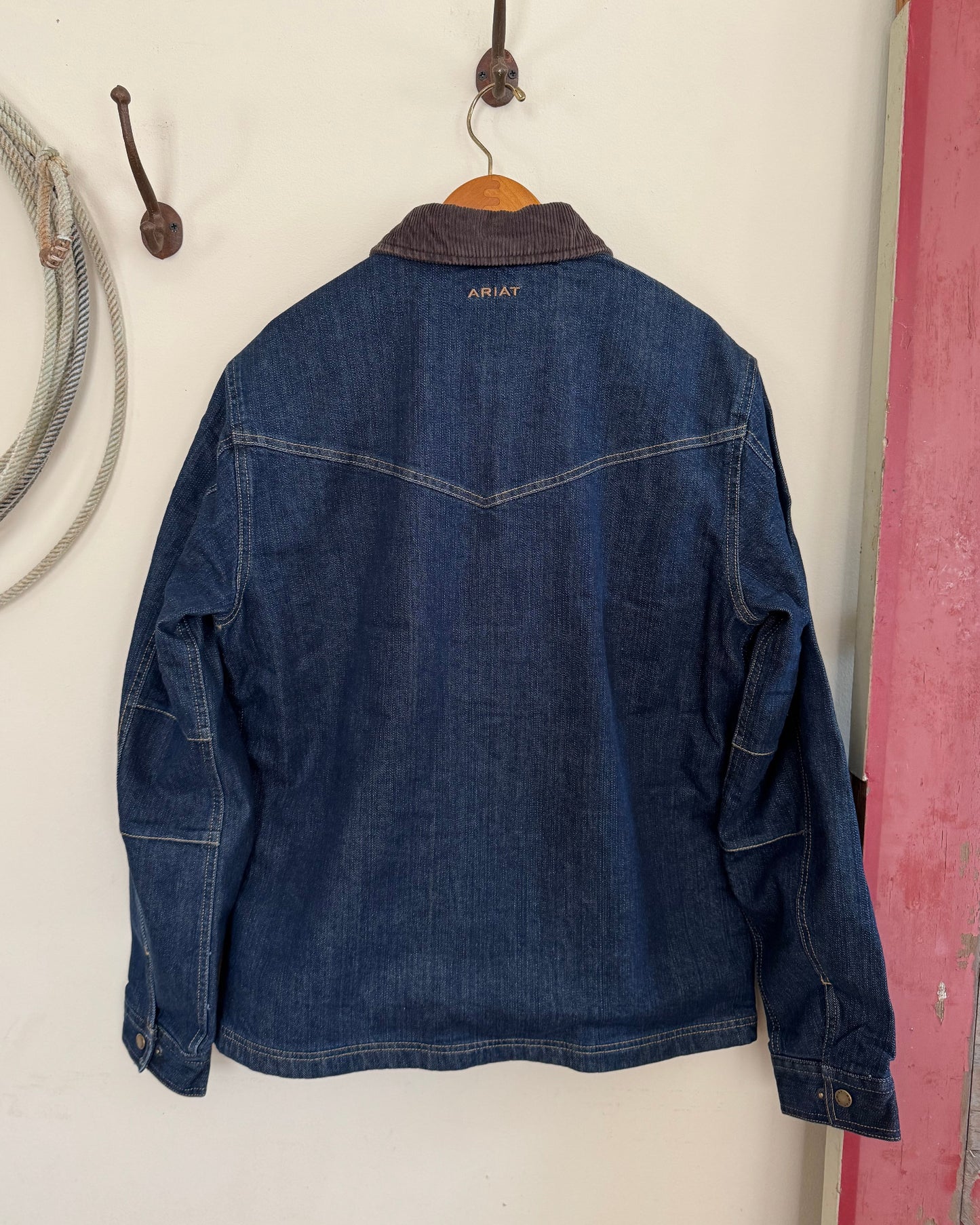 Back view of men's denim jacket hanging on white background
