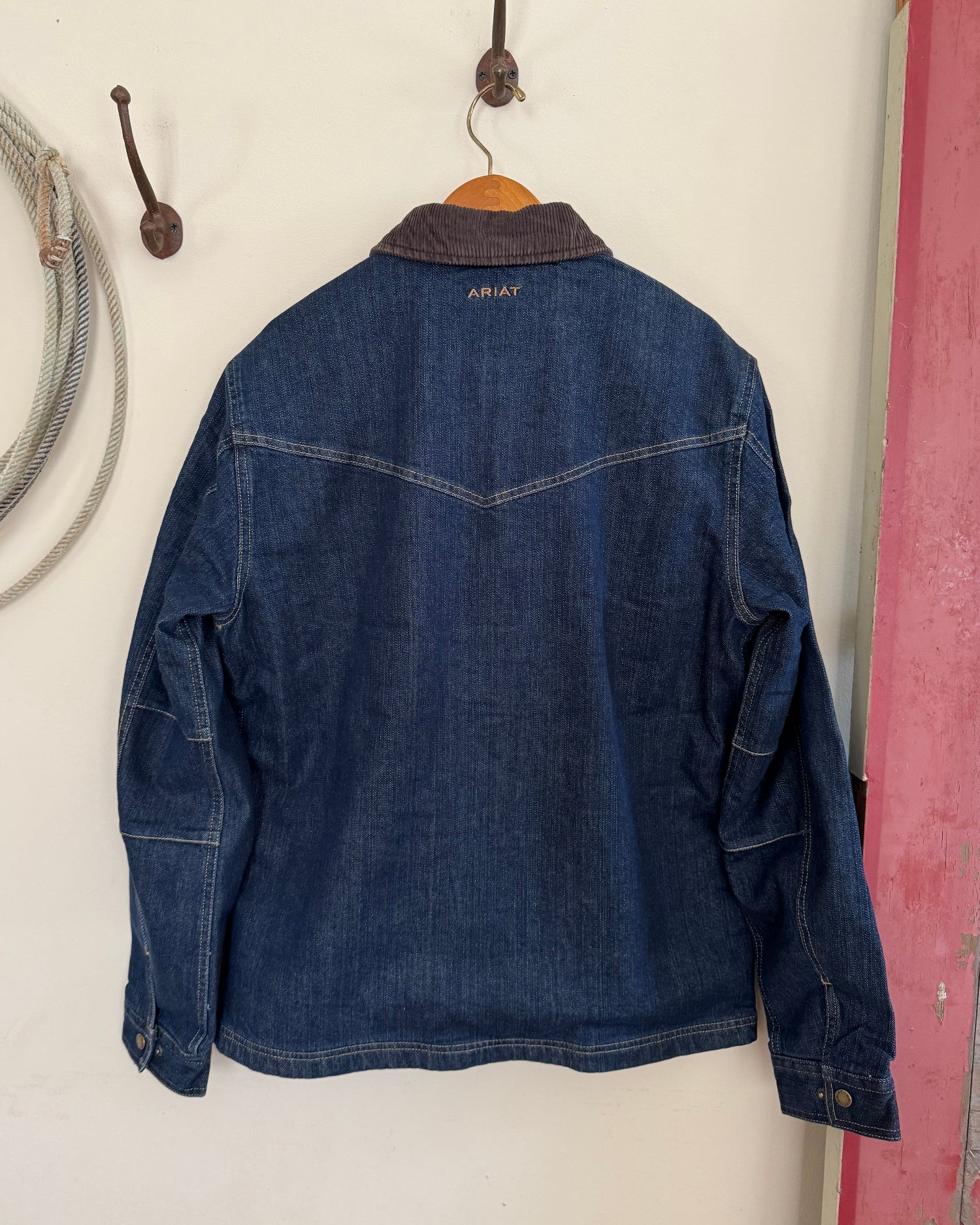 Back view of men's denim jacket hanging on white background