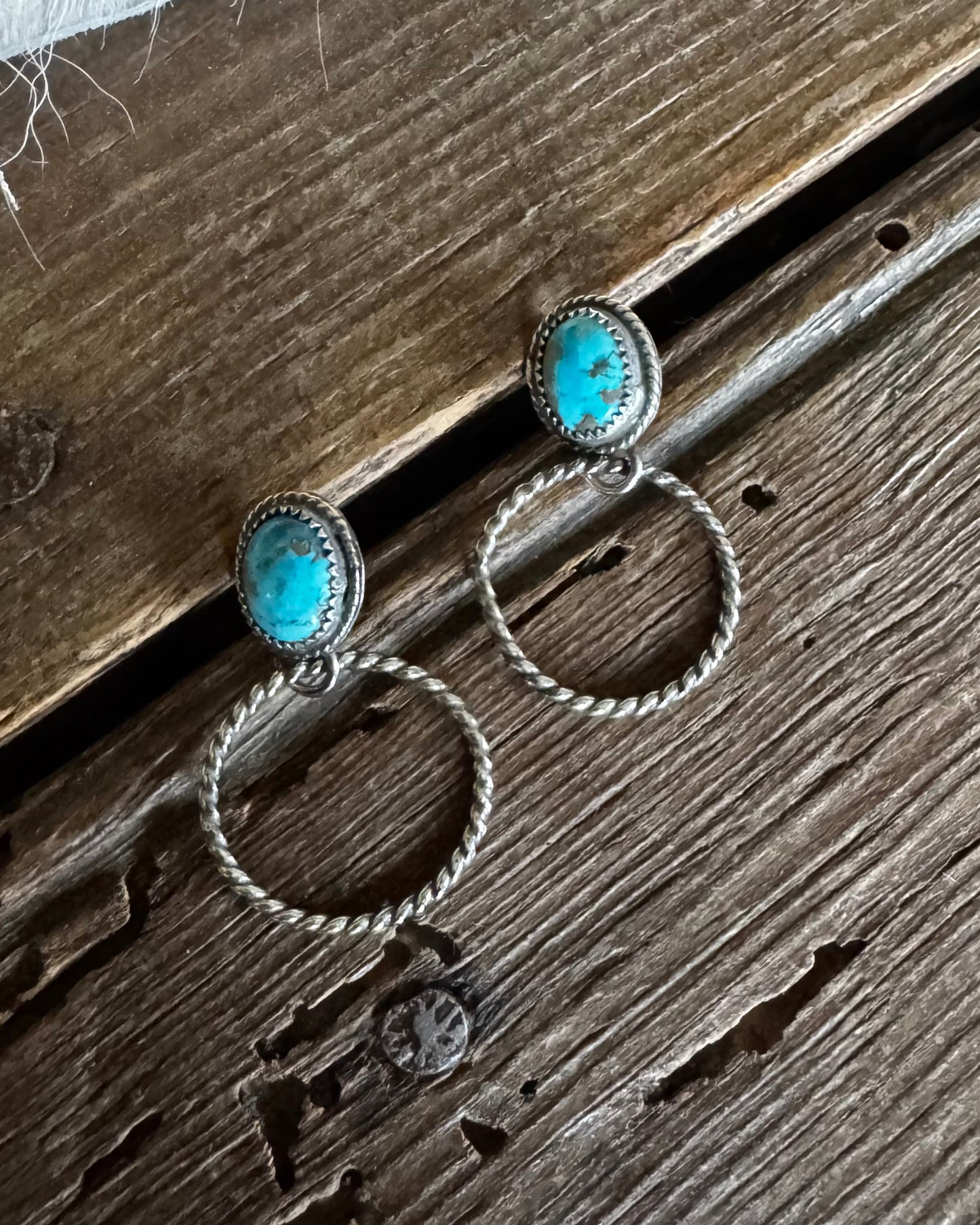 Pair of silver earrings with turquoise stones on a wooden surface