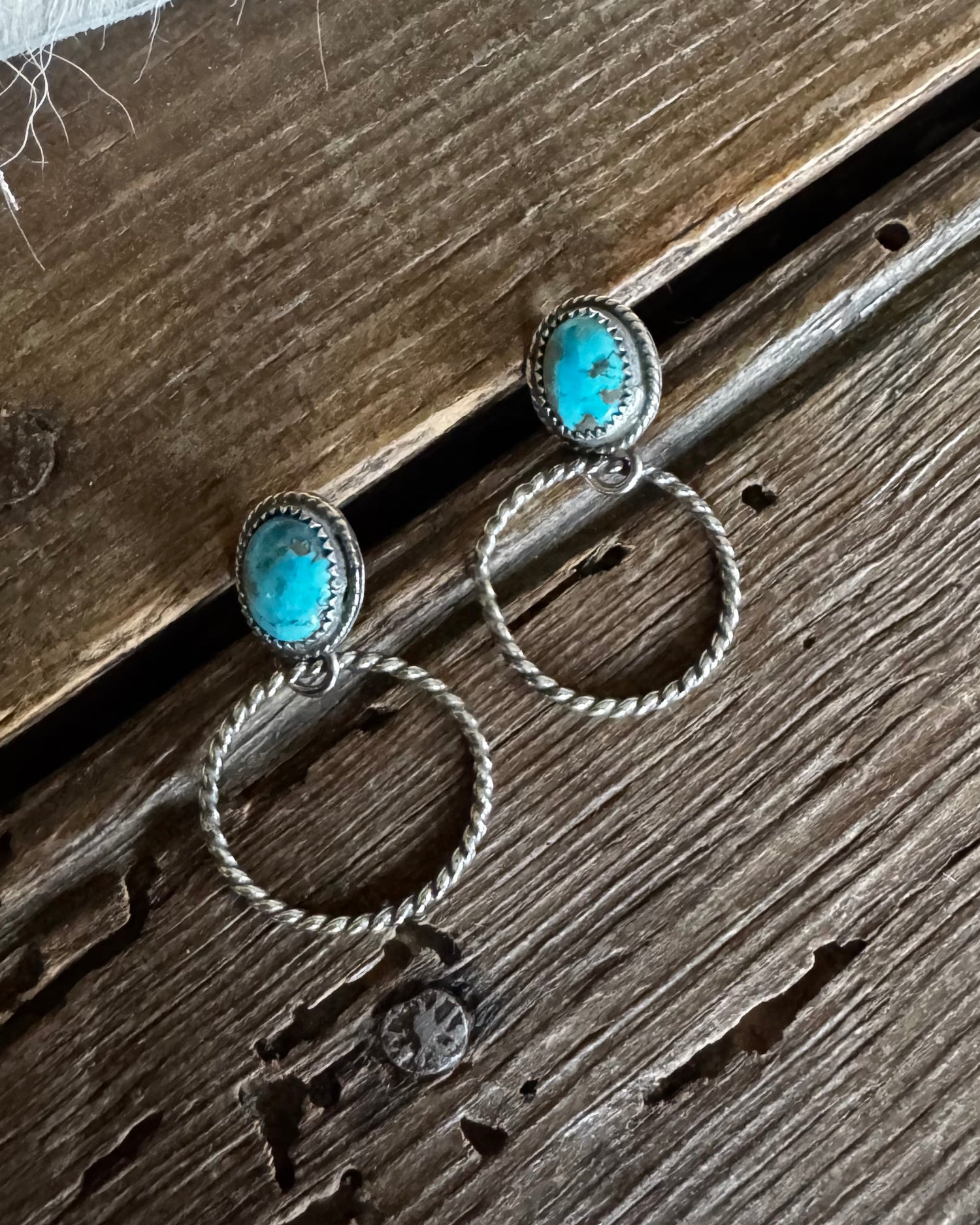 Pair of silver earrings with turquoise stones on a wooden surface