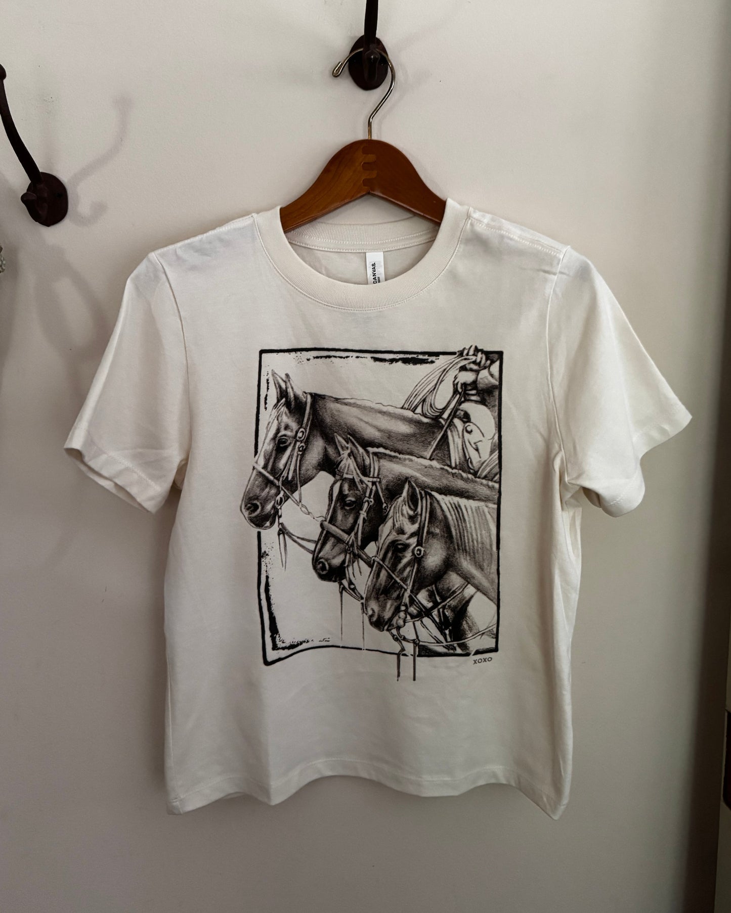 White t-shirt with horse graphic on a hanger against a white wall