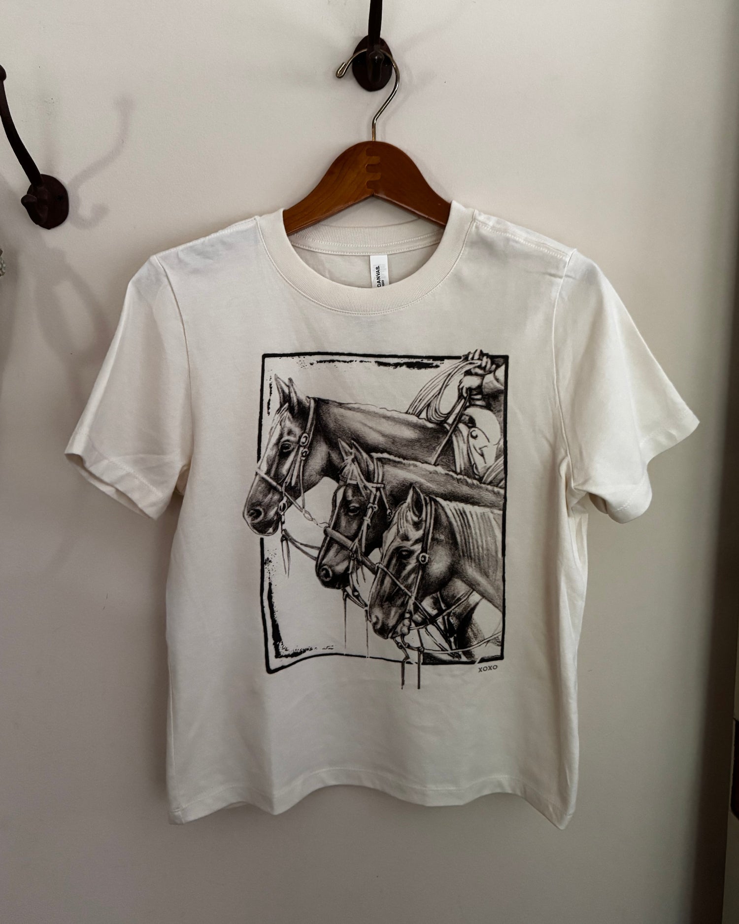 White t-shirt with horse graphic on a hanger against a white wall