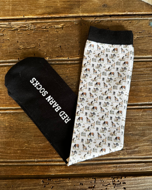 Pair of socks with horse pattern and black sock with 'Red Barn Socks' text on a wooden surface
