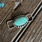 Turquoise stone brooch with silver border on a wooden surface