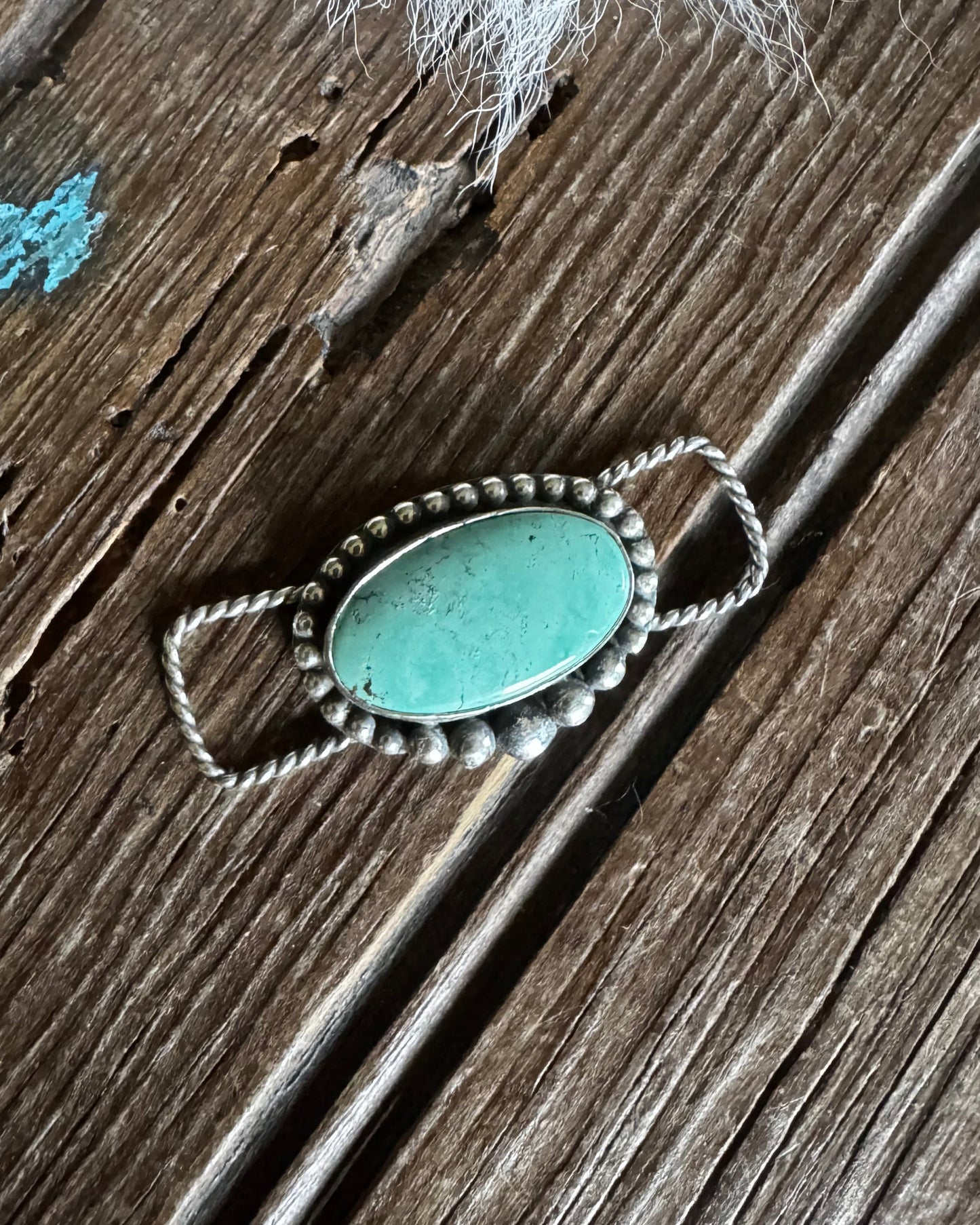 Turquoise stone brooch with silver border on a wooden surface