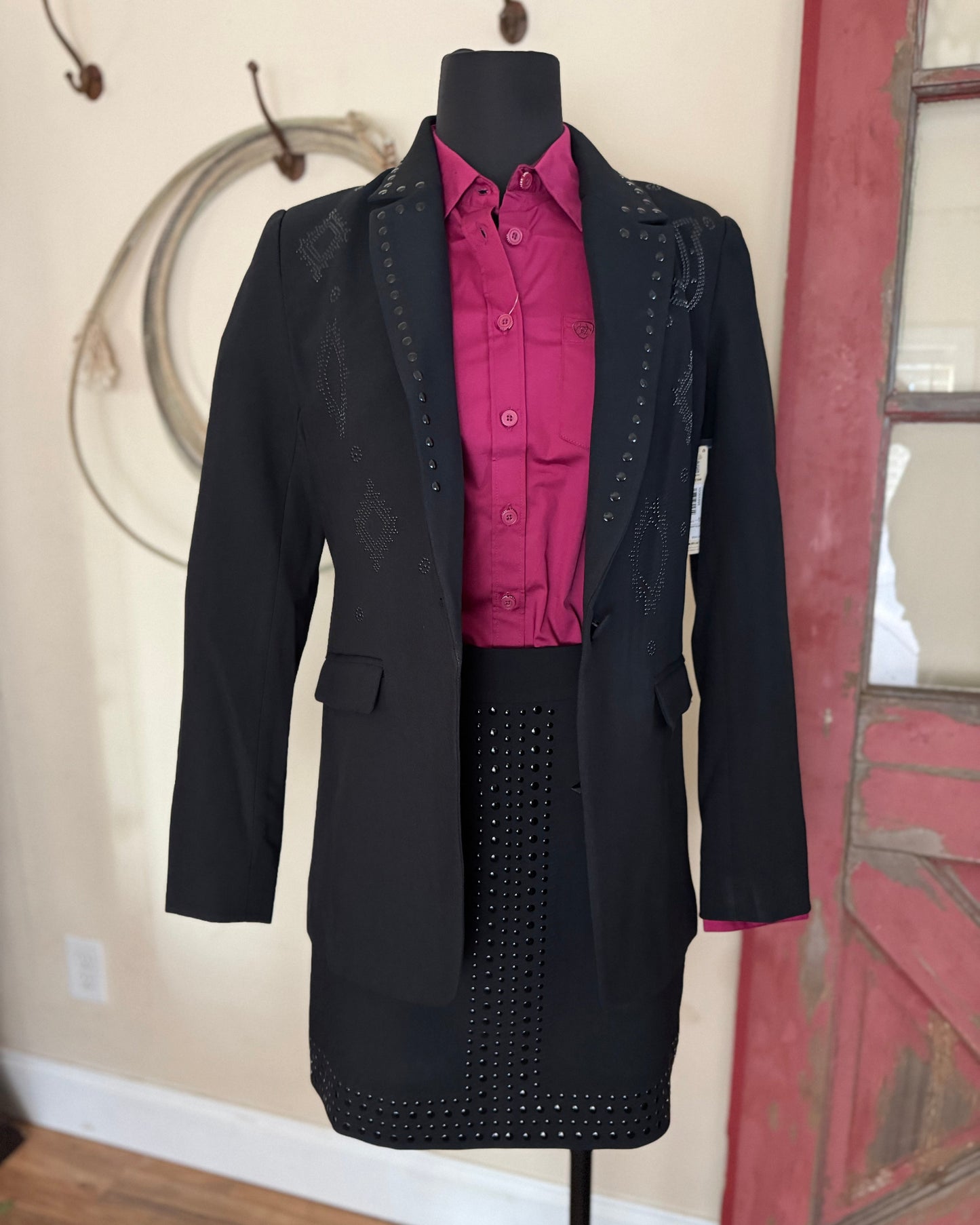 Mannequin wearing a black coat with studded details and a pink shirt against a neutral wall.