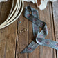 sage patterned scarf on a wooden surface with cowhide leather and rope.