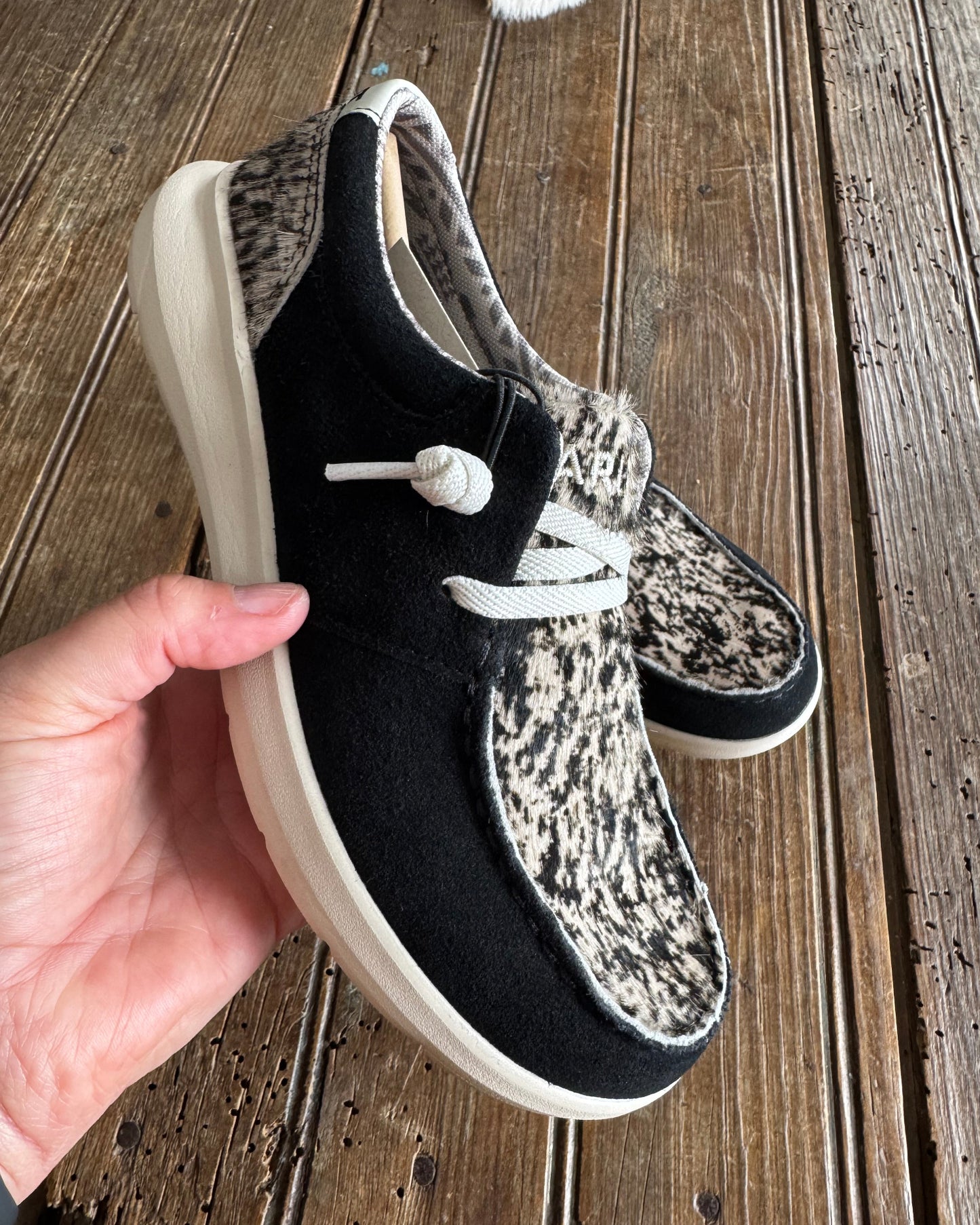 Black and white patterned shoes held against a wooden background