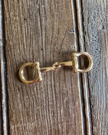 Gold horse bit charm on a wooden surface