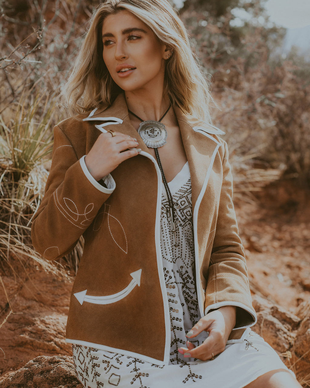 Woman in a brown jacket with white patterns sitting in a natural setting