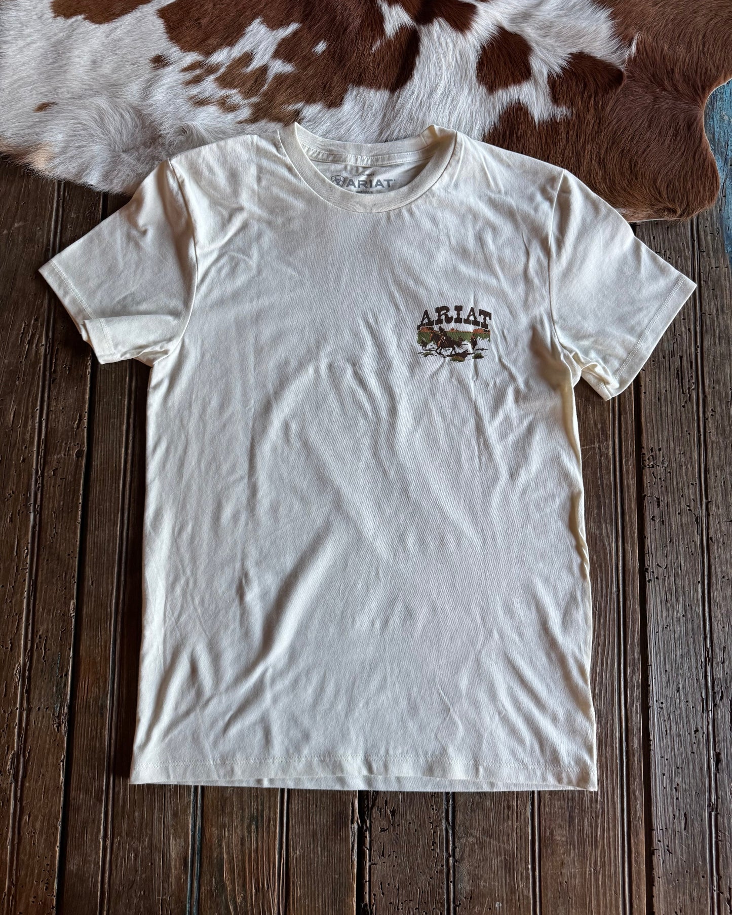 White t-shirt with a logo on a wooden surface with a cowhide rug in the background