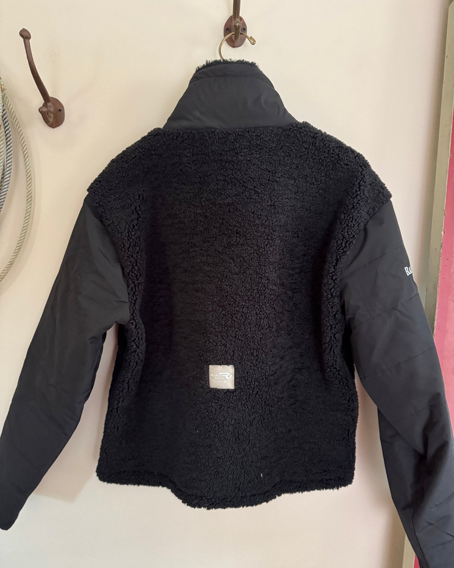 Black jacket with a textured back panel on a hanger against a light background