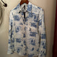 White shirt with blue desert landscape print hanging on a hanger against a beige wall.