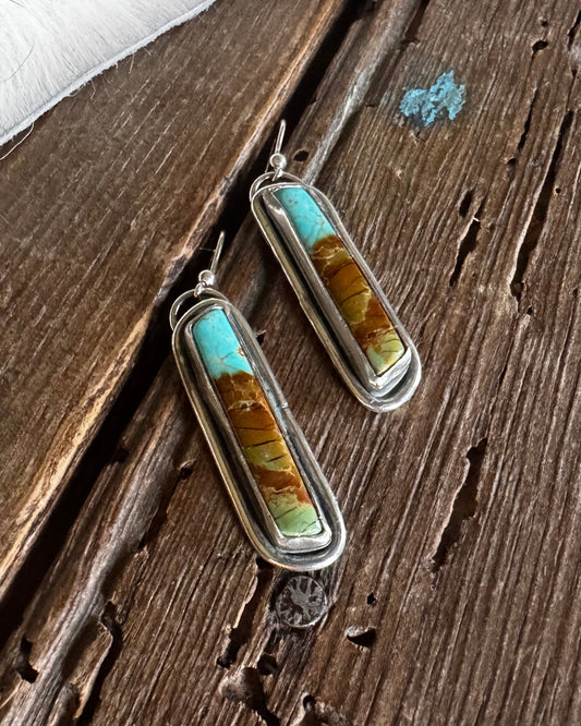 Pair of earrings with turquoise and gold stones on a wooden surface
