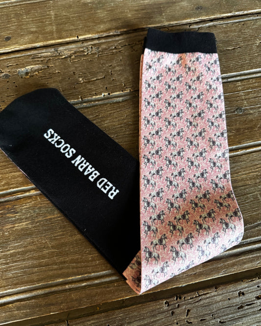 Two pairs of socks, one with a floral pattern and the other black with 'Red Barn Socks' branding, on a wooden surface.