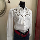 White embroidered shirt on a mannequin with a red belt against a neutral wall.