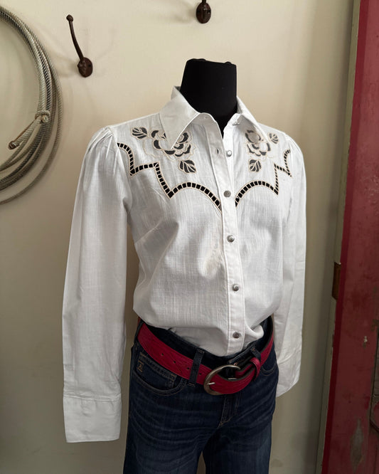 White embroidered shirt on a mannequin with a red belt against a neutral wall.