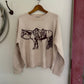 Beige sweater with a black animal design on a wooden hanger against a white wall.
