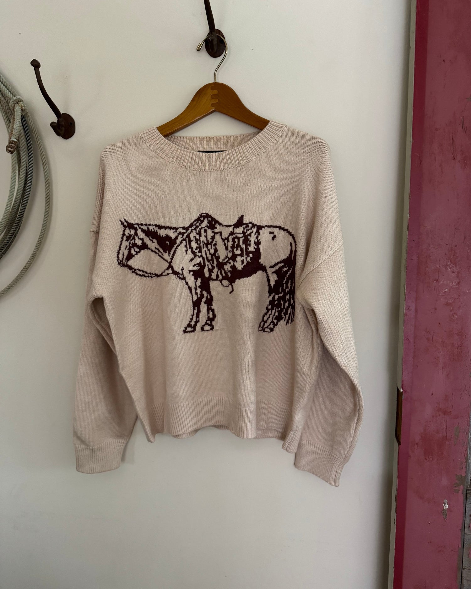 Beige sweater with a black animal design on a wooden hanger against a white wall.