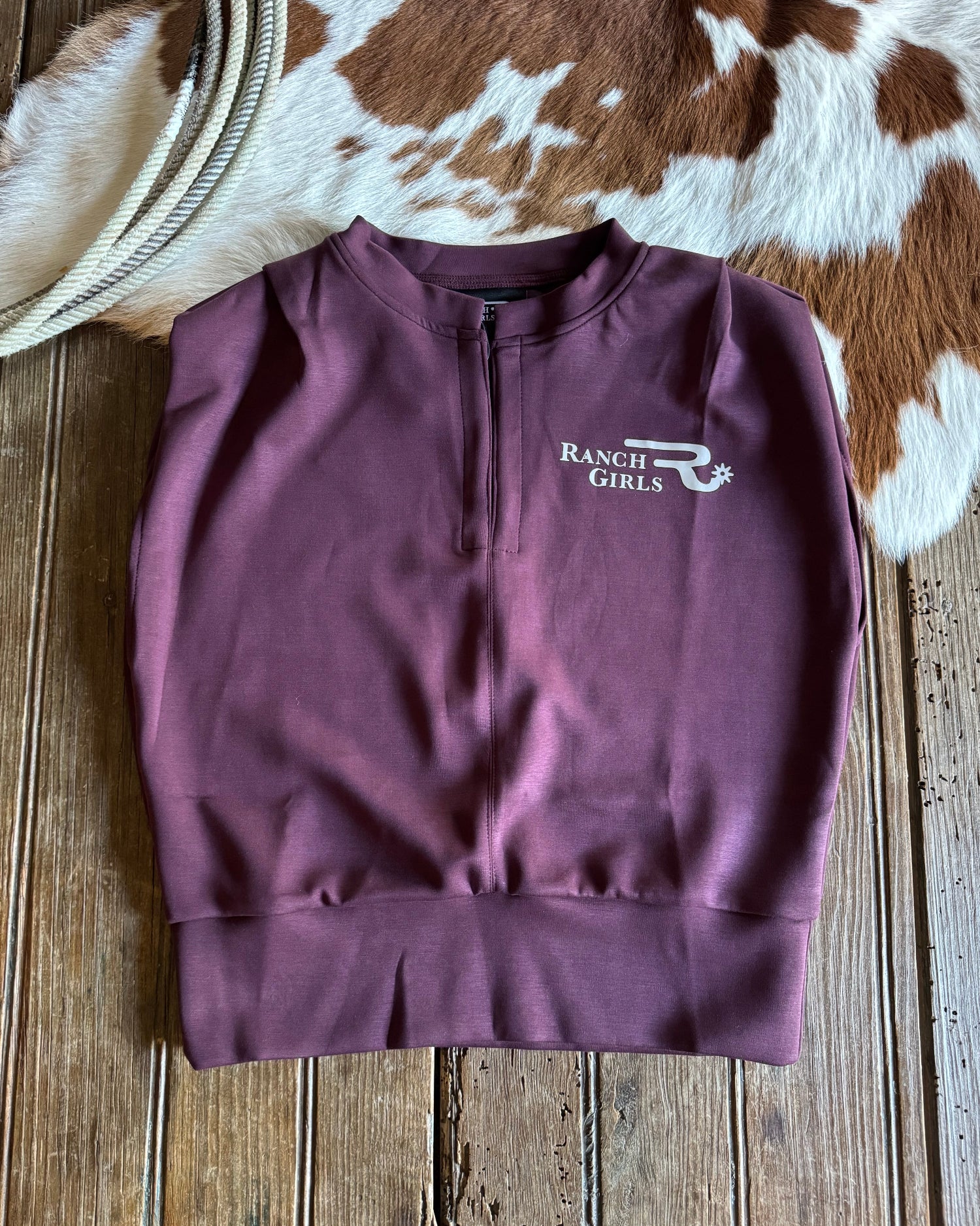 Purple shirt with 'Ranch Girls' logo on a wooden surface with cowhide rug