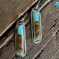 Pair of earrings with turquoise and brown stone on a wooden surface