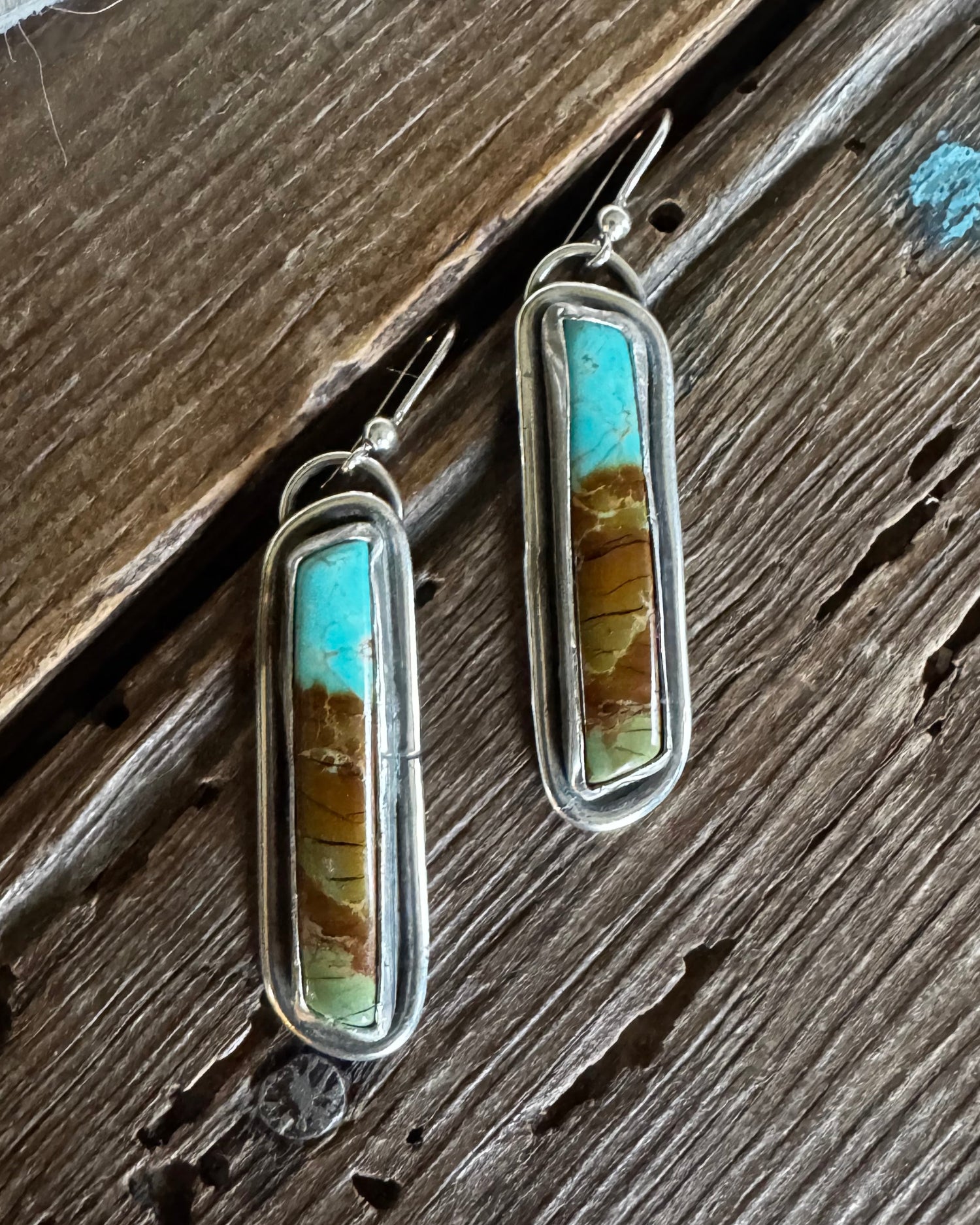 Pair of earrings with turquoise and brown stone on a wooden surface