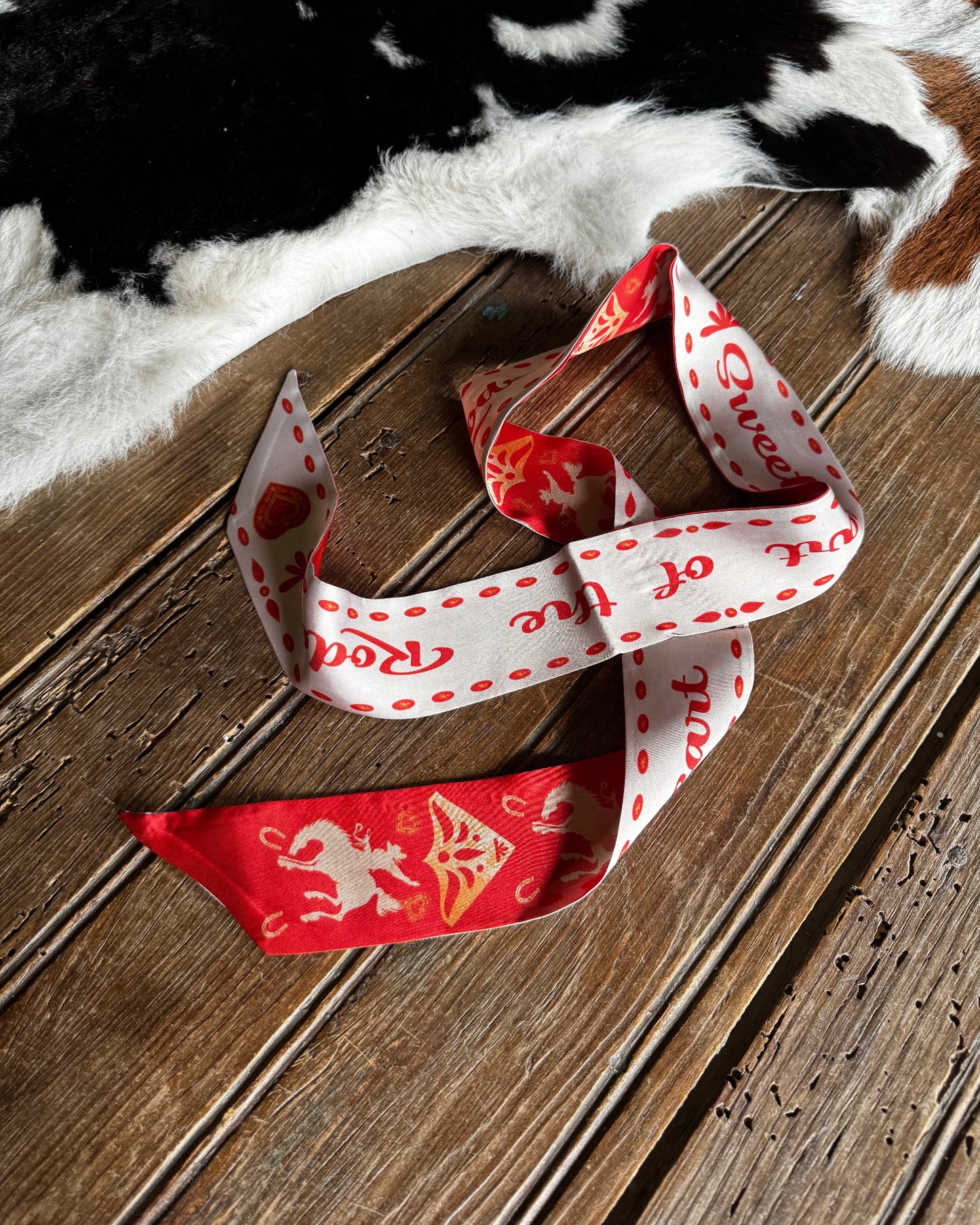 Red and white patterned ribbon on a wooden surface with a cowhide rug in the background