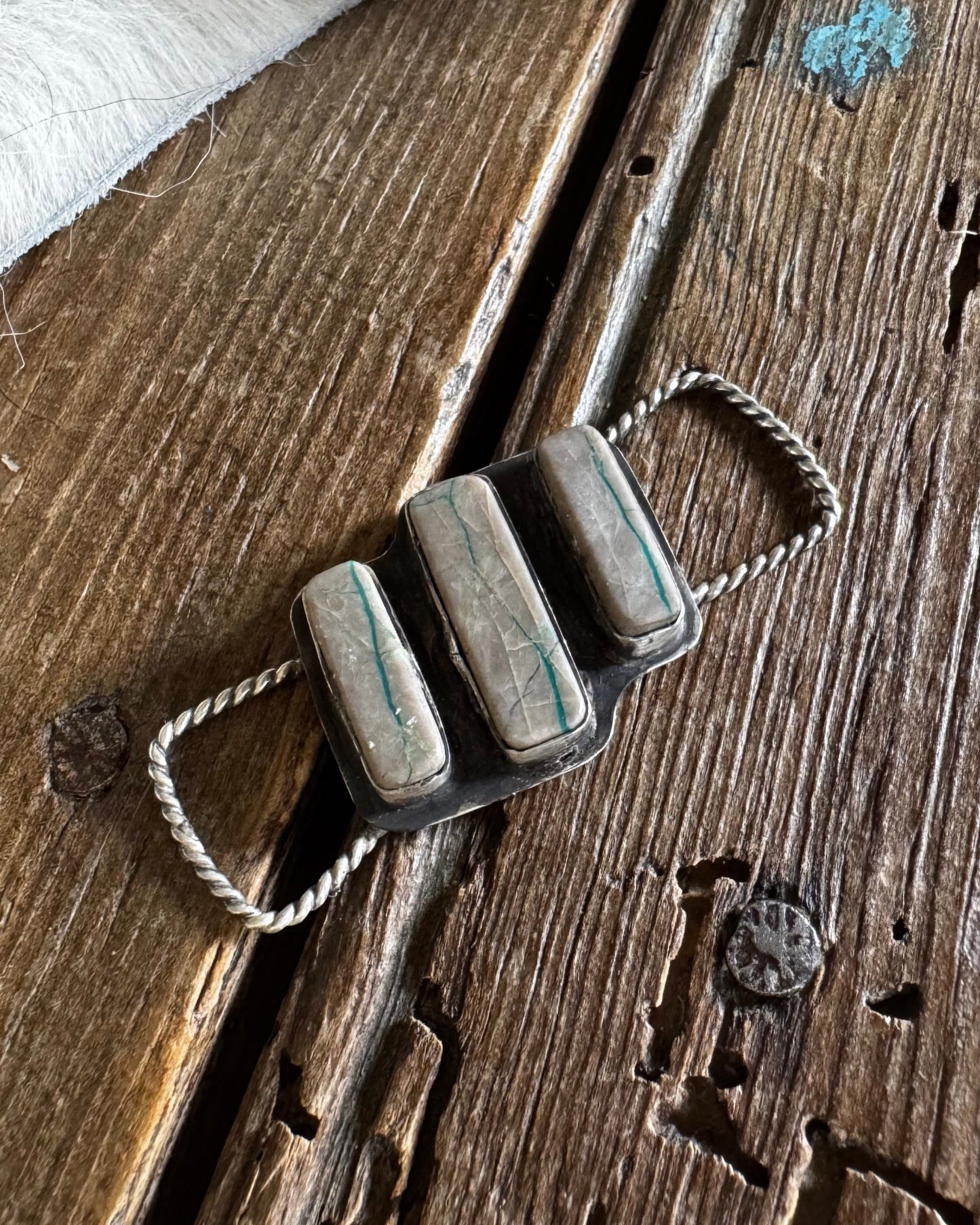Metallic pendant with three cylindrical elements on a wooden surface