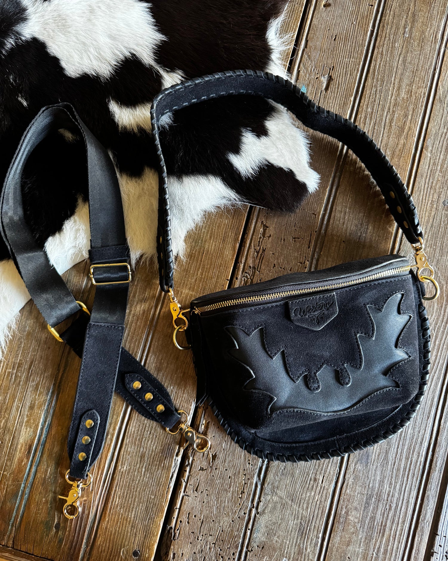 Black leather bag with gold accents on a cowhide rug against a wooden background