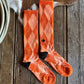 Orange patterned socks on a wooden surface with a cow and rope in the background