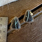 A pair of triangular turquoise and black stone stud earrings with silver-toned bezel settings, displayed on a rustic wooden surface next to a metal ruler for scale.