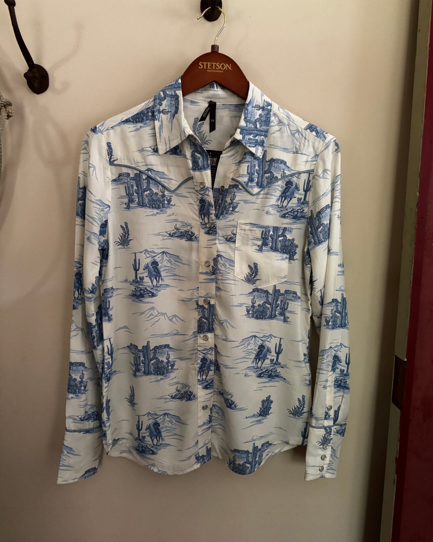 White shirt with blue pattern hanging on a hanger against a beige wall.