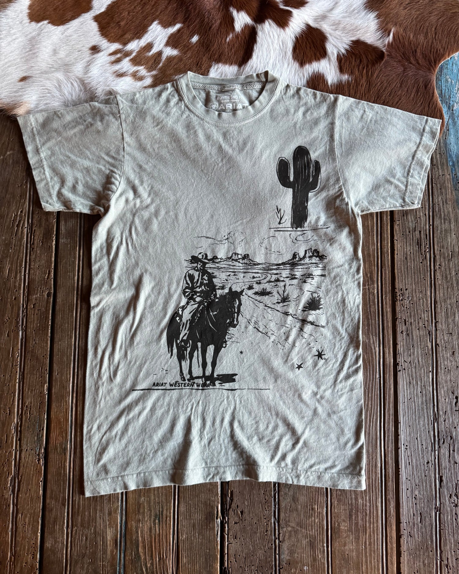 White t-shirt with black graphics on a wooden surface next to a cowhide rug