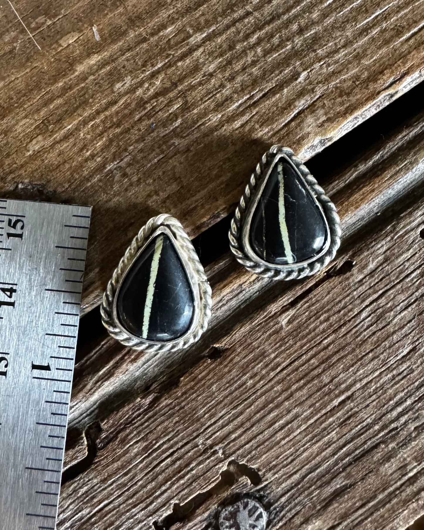 Pair of black and green earrings on a wooden surface with a ruler for scale