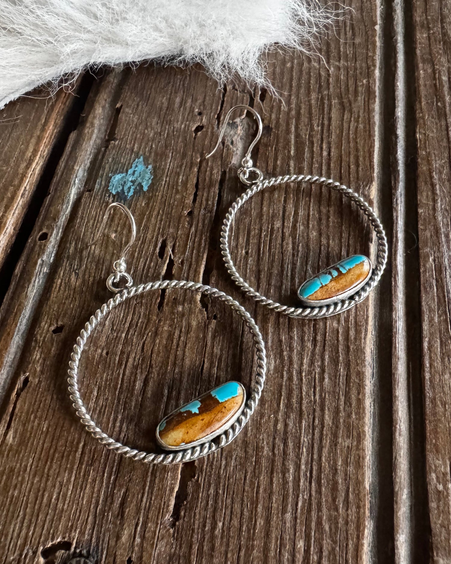 Pair of silver hoop earrings with turquoise stones on a wooden surface.