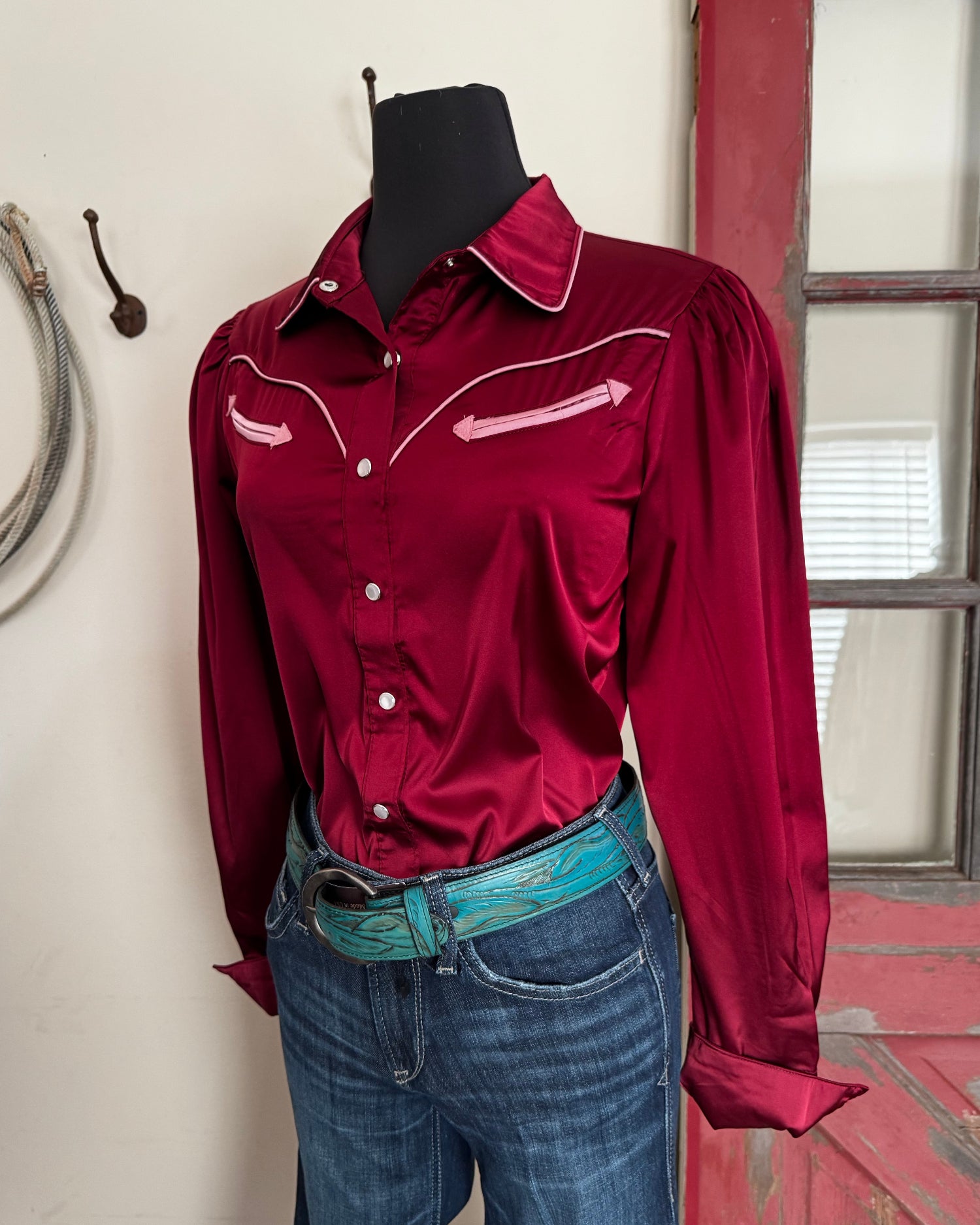 Red blouse with white buttons worn by a mannequin, standing on a wooden floor.