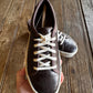Brown leather sneaker with white laces held by a hand on a wooden surface