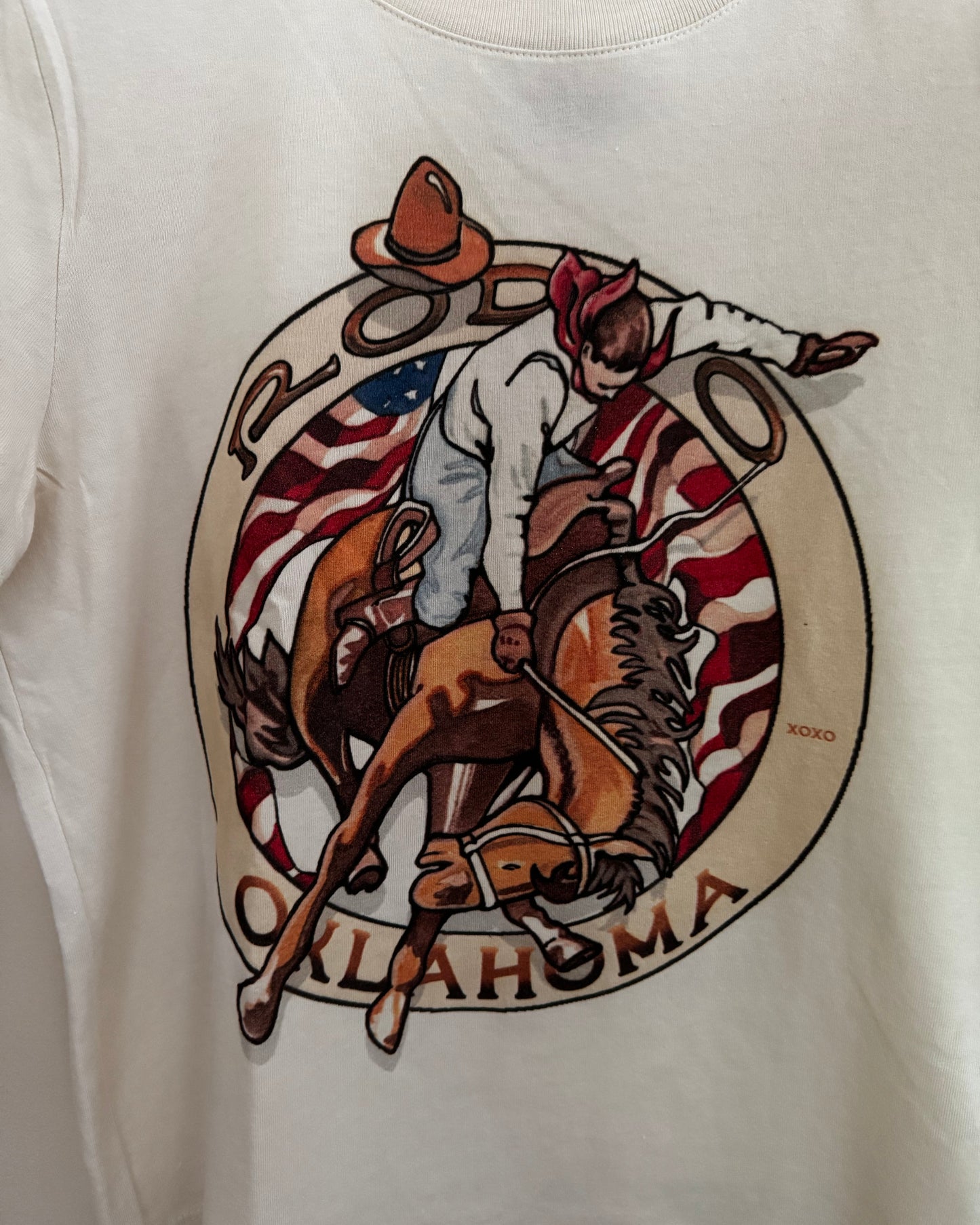 White t-shirt with a graphic of a cowboy riding a bucking bronco, American flag, and 'Oklahoma' text.