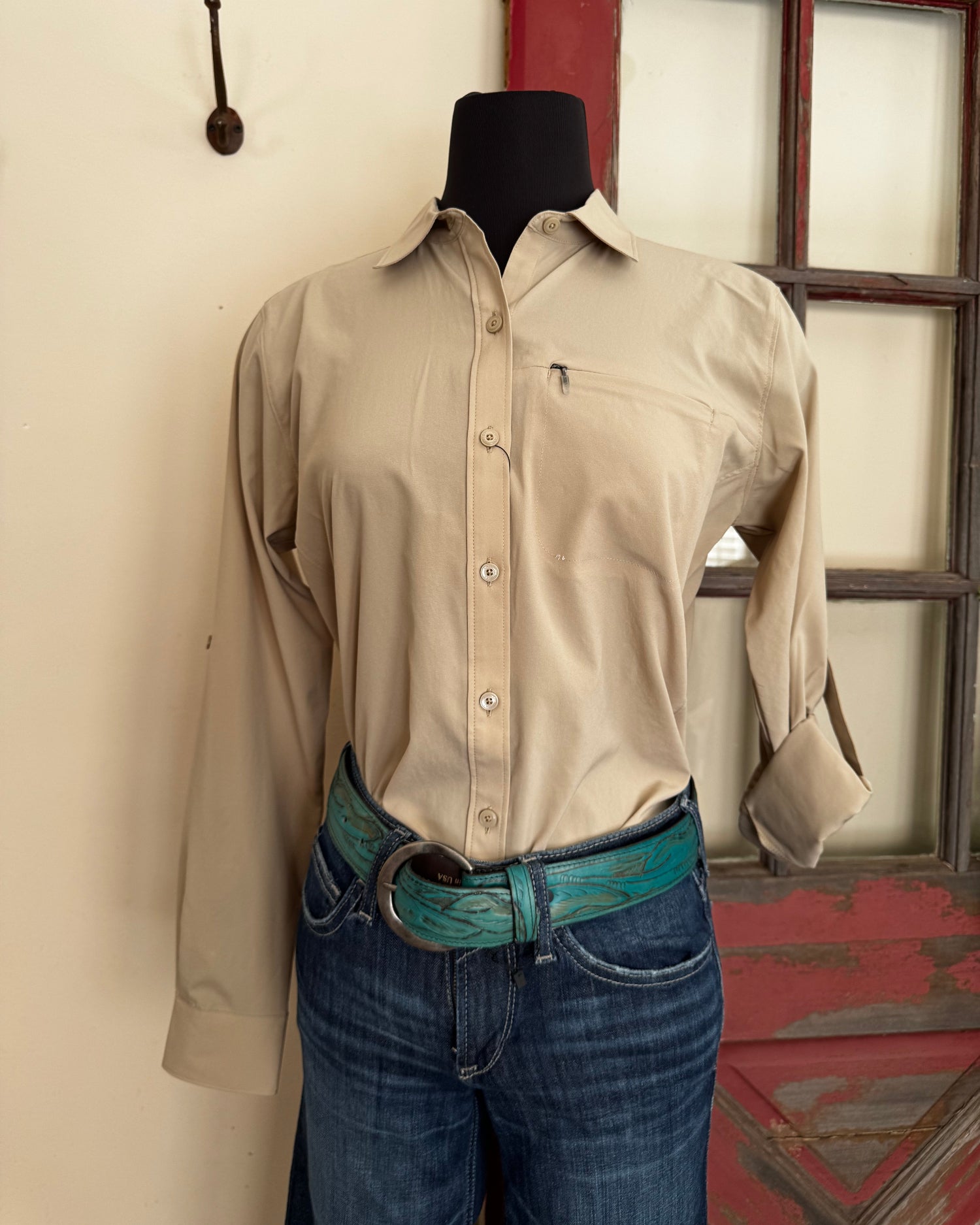 Person wearing a beige shirt and blue jeans standing against a red and white wall.