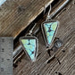 Two triangular turquoise drop earrings with silver bezel settings and fishhook wires, displayed on a rustic wooden surface next to a metal ruler for scale.