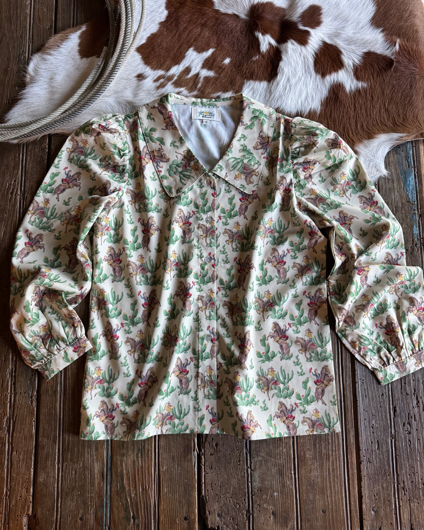 Retro cowboy and cactus patterned shirt on a wooden surface with a cowhide rug