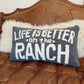Decorative pillow with 'Life is better on the ranch' text on a brown leather couch.