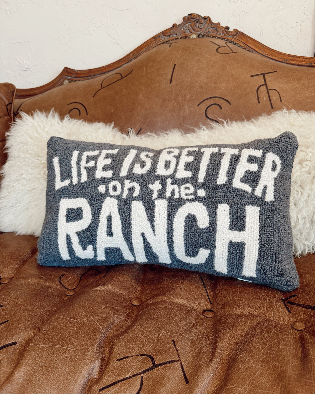 Decorative pillow with 'Life is better on the ranch' text on a brown leather couch.
