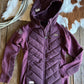 Purple quilted jacket on a wooden surface with a cowhide rug in the background