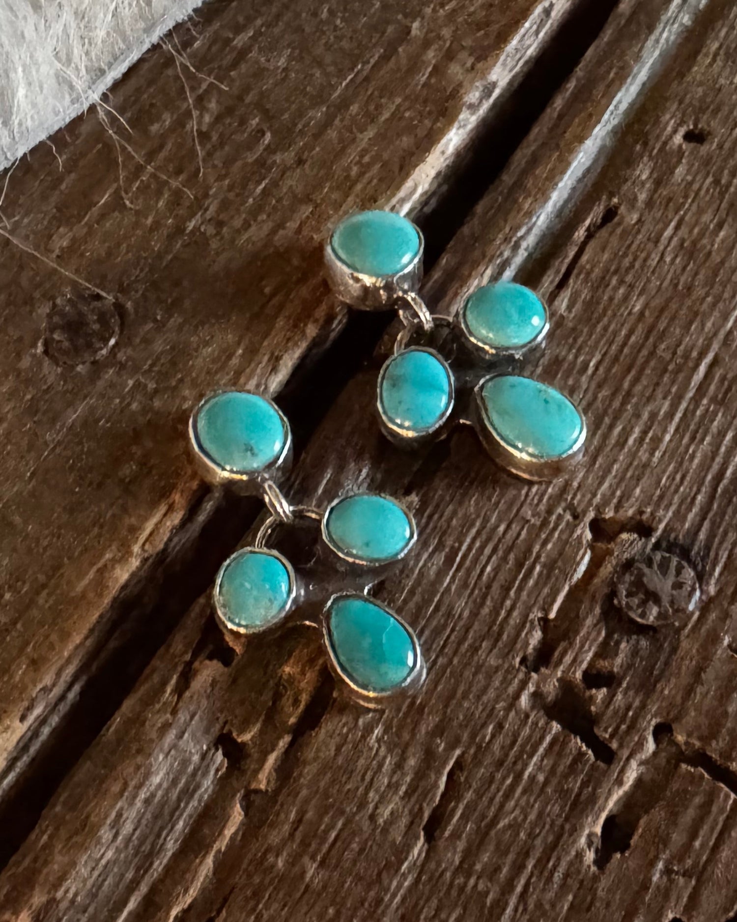 A pair of gold-toned earrings with multiple oval turquoise stones, displayed on a rustic dark wood surface with a white fur trim visible in the top left corner.