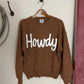 Brown sweater with 'Howdy' text on a white surface
